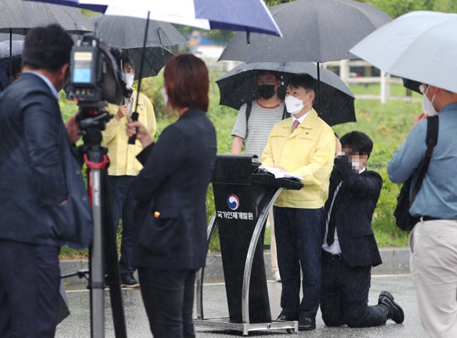 27일 오전 강성국 법무부차관이 진천 공무원인재개발원 앞에서 브리핑을 하는 동안 공무원 한 명이 무릎을 꿇고 우산을 받쳐들고 있다. <사진 연합뉴스>